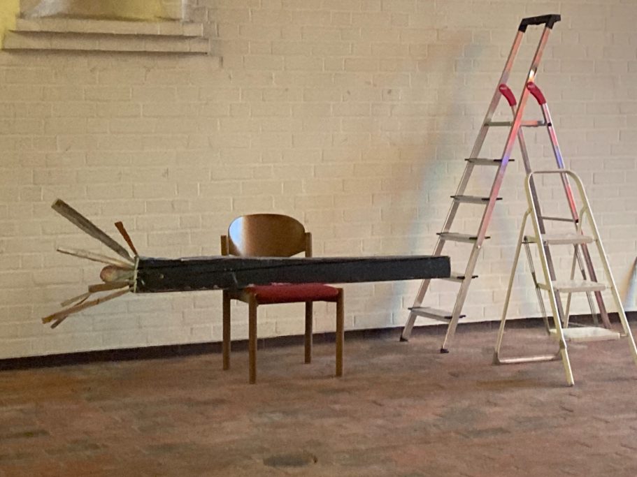 Ein Stuhl neben einer Leiter mit einem langen, schwarzen Balken und mehreren herausragenden Stäben.