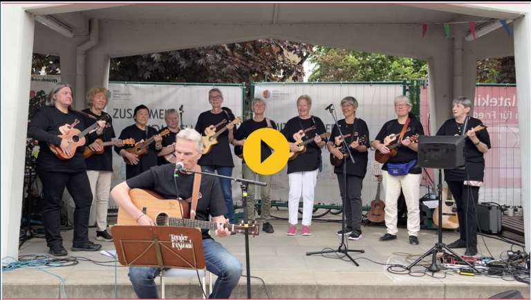 Eine Musikgruppe spielt auf Ukulelen und Gitarre. Sänger mit Notenständer im Vordergrund.