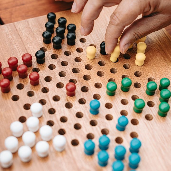 Bunte Spielfiguren auf einem Holzbrett, einige Figuren werden bewegt.