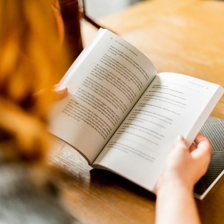 Eine Person liest ein Buch mit einem offenen Text auf einem Holztisch.