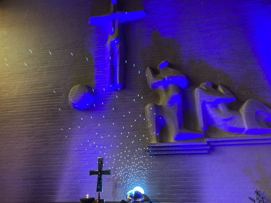 Kunstvolle Wandgestaltung mit Kruzifix und Figuren in blauem Licht.