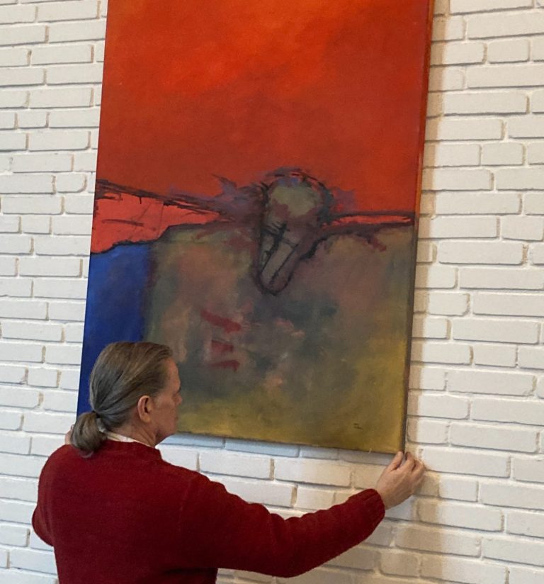 Mann steht neben abstrakten Gemälden mit verschiedenen Farben und Figuren im Hintergrund.