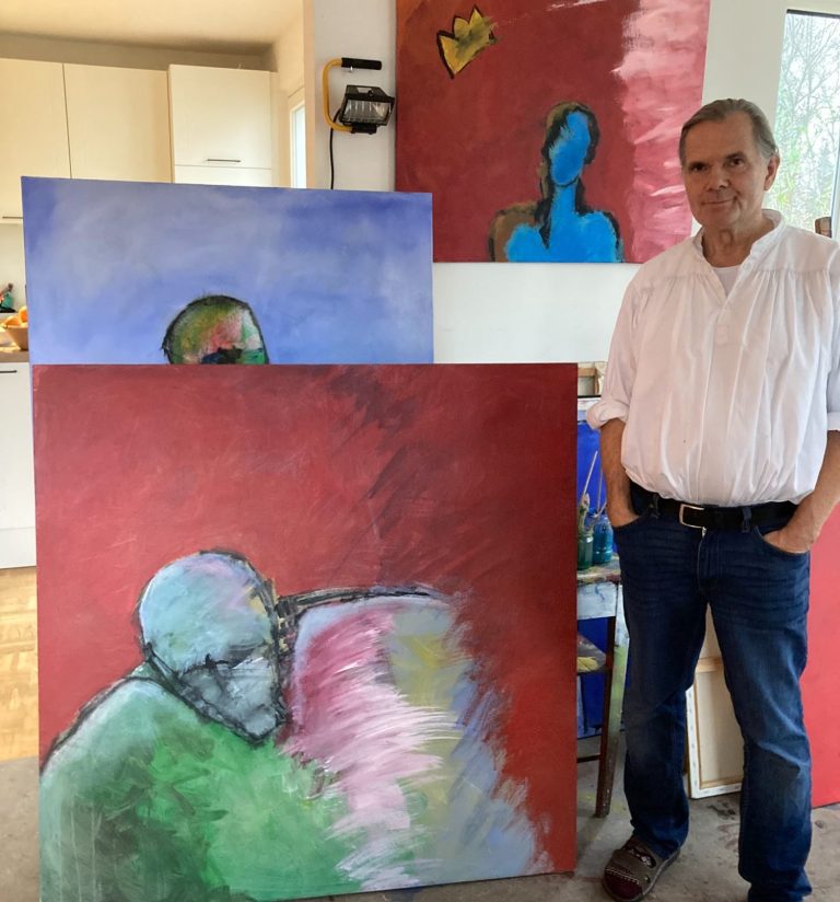 Mann steht neben abstrakten Gemälden mit verschiedenen Farben und Figuren im Hintergrund.