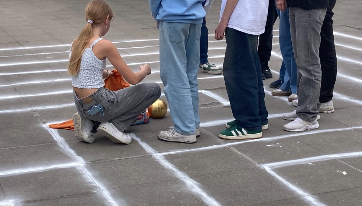 Gruppe von Menschen, die auf einem markierten Spielfeld stehen; eine Person spielt mit einem Ball.