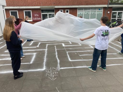 Gruppenaktivität auf dem Boden mit einem transparenten Tuch und einem labyrinthartigen Muster.