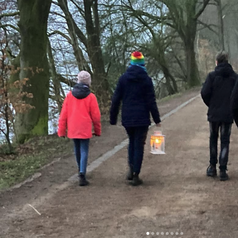 Drei Personen spazieren einen Weg entlang, eine hält eine Laterne.