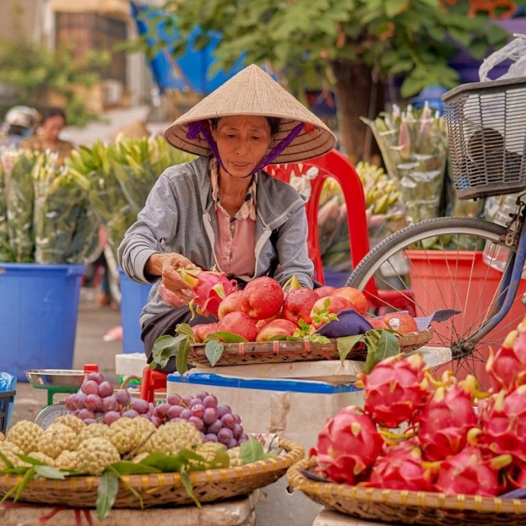 Frau mit traditionellem Hut verkauft frische Früchte an einem Marktstand.
