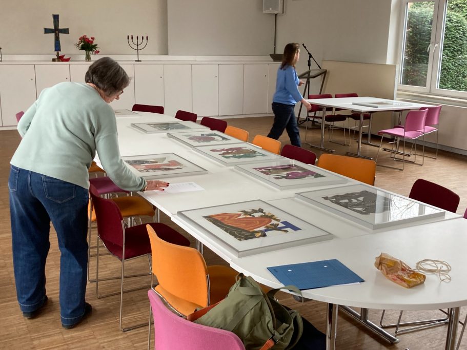 Zwei Personen arrangieren Bilder auf einem langen Tisch in einem hellen Raum.