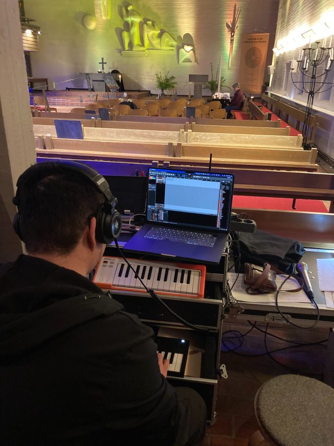 Person mit Kopfhörern spielt Klavier, vor einem Laptop in einem hellen Raum.